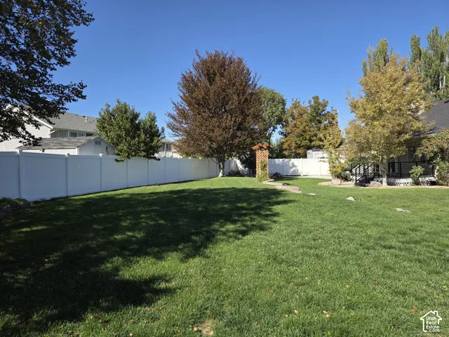 Expansive backyard featuring a large grass lawn, white vinyl fencing, mature trees, a wooden pergola, and stone landscaping accents