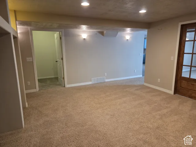 Neutral interior space featuring recessed ceiling lighting, wall-mounted sconces, carpeted flooring, built-in shelving, and a wood-frame glass panel door