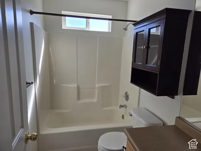 Bathroom featuring a molded composite tub and shower surround, wall-mounted dark wood-finish cabinet, neutral-toned countertop, and a large vanity mirror