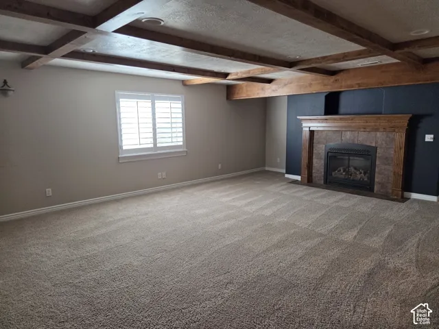 Coffered ceiling with exposed wood-finish beams, fireplace featuring a decorative wood mantel and tile surround, plantation shutters, and wall-to-wall carpeting