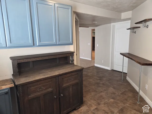 Blue-painted wall cabinetry, dark stained wood hutch with intricate carved detailing, tile flooring, and live-edge wood shelving with industrial-style metal piping supports