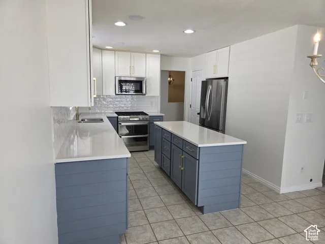 Kitchen featuring white upper cabinetry, blue lower cabinetry with horizontal shiplap detailing, solid-surface countertops, subway tile backsplash, and stainless steel appliances