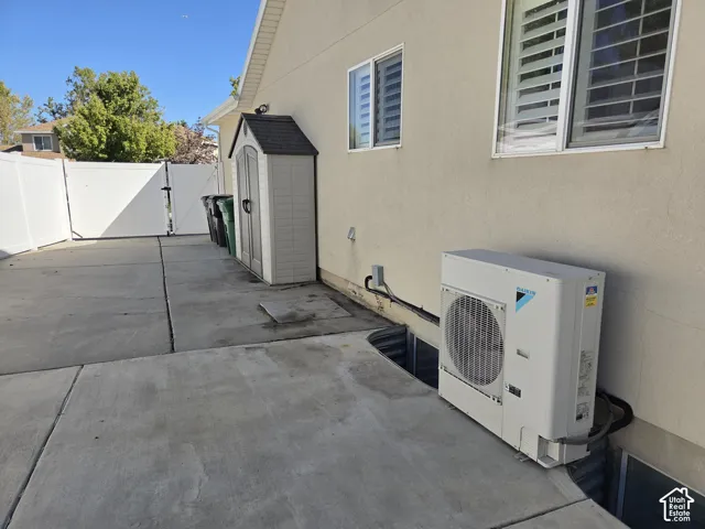 Concrete side yard featuring a white vinyl privacy fence, egress window well, and an exterior HVAC unit