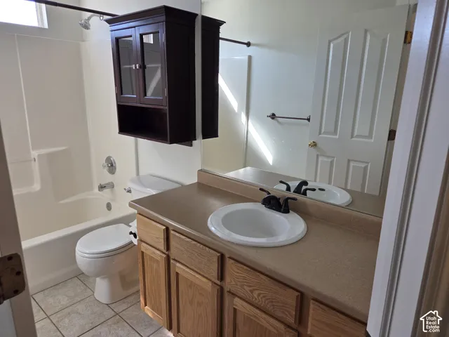 Bathroom featuring a wood-finish vanity with a matte countertop, drop-in sink with a dark-finish faucet, wall-mounted cabinet with glass-panel doors, and tile flooring
