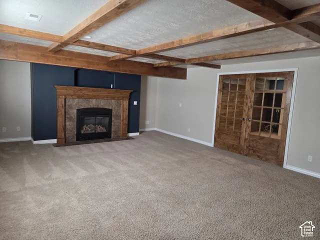 Coffered ceiling with stained wood beams, fireplace with a stone-surround mantle, and stained wood French doors with glass panes