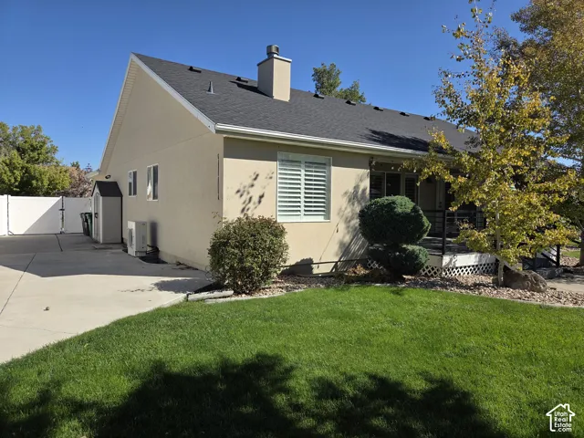 Stucco exterior featuring an asphalt shingle roof, chimney, concrete driveway, white vinyl fencing, and a raised rear deck