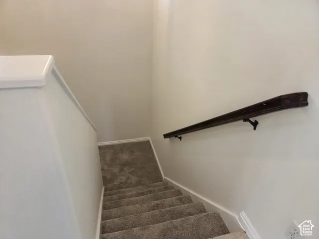 Staircase featuring wall-to-wall carpeting and a dark-finish wood handrail with decorative metal brackets
