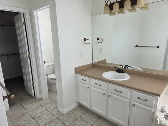 White cabinetry with metallic hardware, solid-surface countertop, integrated basin, wall-to-wall mirror, and tile flooring