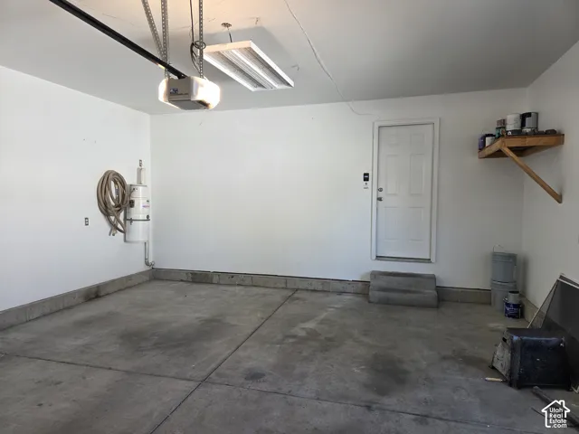 Garage featuring smooth-finish concrete flooring, built-in central vacuum system, fluorescent overhead lighting, and fixed wood shelving