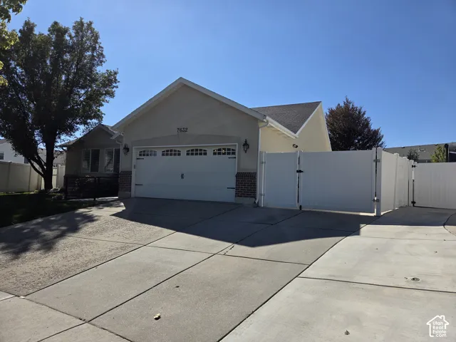 Single-story residence featuring a stucco and brick exterior, an attached two-car garage with overhead carriage-style doors, and expansive gated side yard access