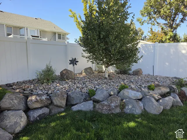 Backyard featuring a tiered natural boulder retaining wall, xeriscaped rock garden, mature tree, and full-height vinyl privacy fencing
