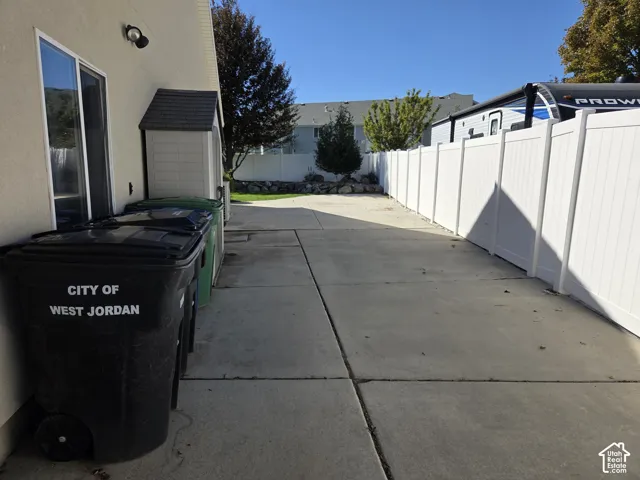 Concrete side yard featuring full-height white vinyl perimeter fencing and an exterior storage shed