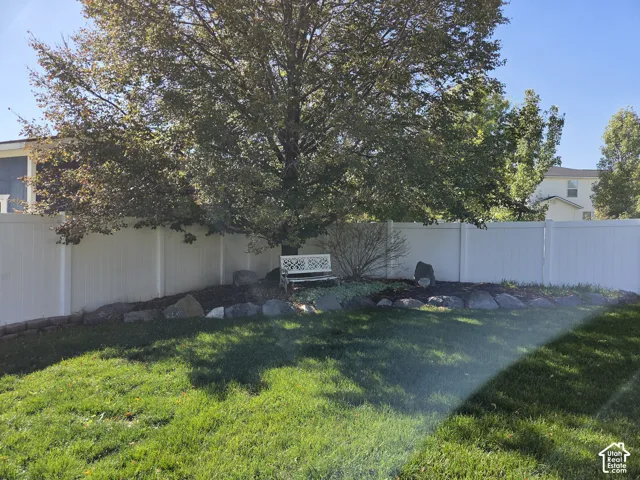Backyard featuring a white vinyl privacy fence, mature shade tree, stone landscape edging, and mulched garden beds