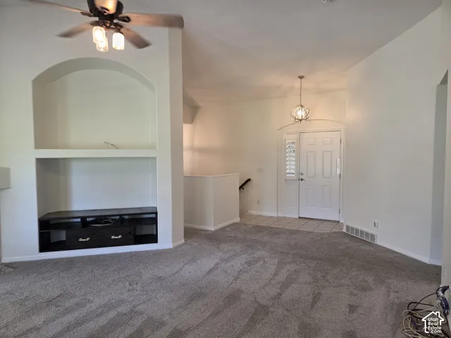 Vaulted ceilings, built-in arched media niche with cabinetry, polished-nickel chandelier, and entryway with tile flooring