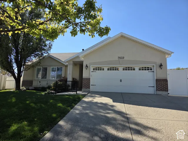 Single-story exterior featuring light-toned siding, brick accents, a gabled roofline, a two-car garage with overhead carriage-style windows, and a concrete driveway