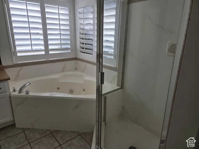 Corner jetted soaking tub with tile surround, glass-enclosed shower, and plantation shutters