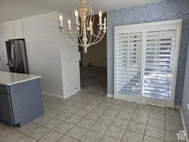 Kitchen island with blue shiplap paneling and quartz countertop, decorative metal chandelier, sliding glass door with plantation shutters, and patterned wall covering