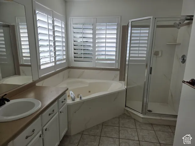 Bathroom featuring a corner jetted soaking tub with tile surround, a glass-enclosed shower, dual-window plantation shutters, and a vanity with an integrated basin