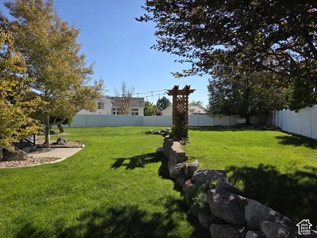 Expansive backyard featuring a grass lawn, decorative stone retaining wall, wooden arbor, and full-perimeter vinyl fencing