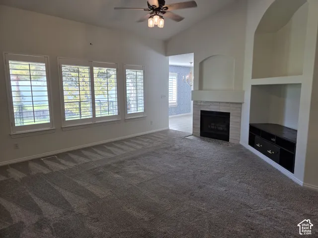 Vaulted ceilings, a stone-surround fireplace, built-in shelving, triple-pane windows with plantation shutters, and a ceiling fan with integrated lighting