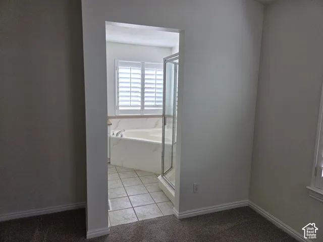 Bathroom featuring a soaking tub with tile surround, a glass-enclosed shower, neutral floor tiling, and interior window shutters