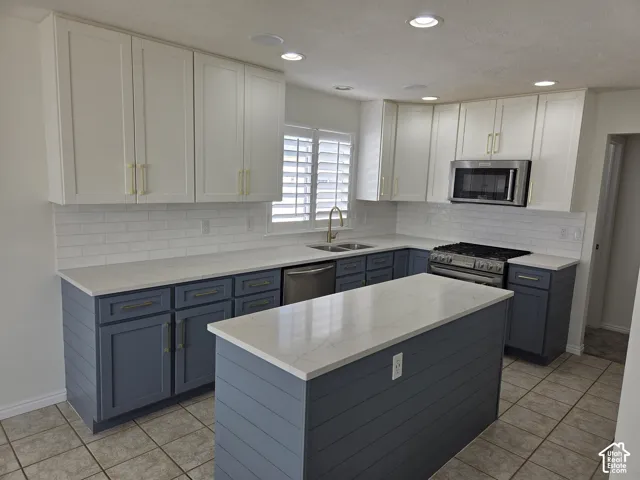 Kitchen featuring two-tone cabinetry with shiplap detailing on the lower cabinets and island, stone-finish countertops, subway tile backsplash, and stainless steel appliances