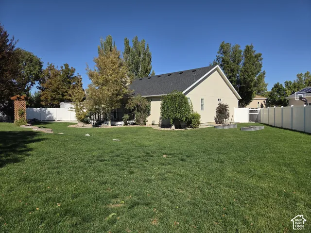 Expansive backyard featuring a large grass lawn, white vinyl perimeter fencing, mature trees, and a decorative wooden pergola
