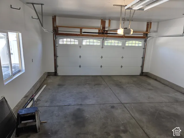 Attached two-car garage featuring a sectional door with windows, concrete flooring, overhead automatic opener, and built-in upper shelving