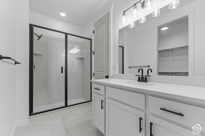 Bathroom featuring a white vanity with a composite countertop, matte black hardware, a walk-in shower with a glass enclosure, and stone-finish tile flooring