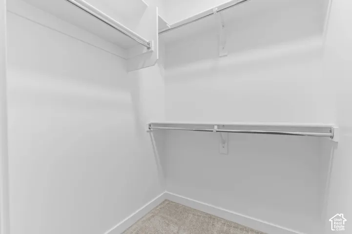 Walk-in closet featuring tiered white shelving and dual chrome garment rods over neutral carpeting