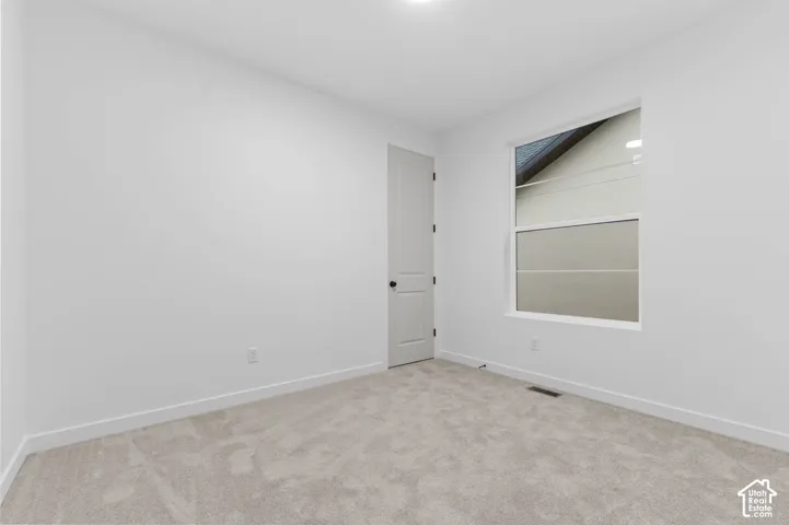 Neutral interior space featuring neutral wall-to-wall carpeting, crisp white walls, a single-panel interior door with matte black hardware, and a double-pane window