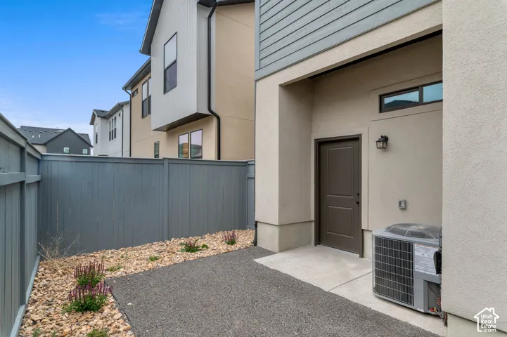 Modern townhome entry featuring a concrete patio, metal perimeter fencing, decorative rock landscaping, and a dark-finish entry door with sidelighting