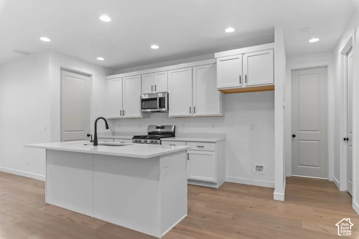 Kitchen featuring white shaker-style cabinetry, quartz countertops, a central island with a matte black faucet, stainless steel appliances, and wood-finish flooring
