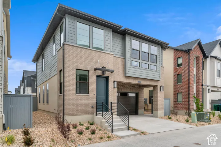 Contemporary exterior featuring a combination of light-toned brick masonry and horizontal siding, a covered garage entry, multi-pane windows, and concrete front steps with metal railings