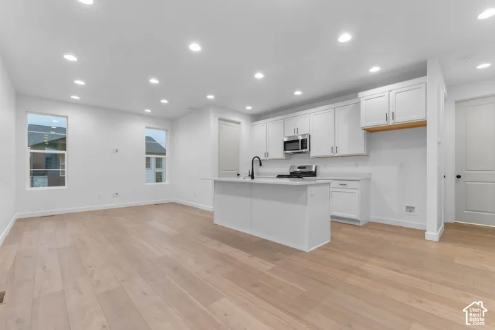 Kitchen featuring white cabinetry, an island with a sink, stainless steel appliances, recessed lighting, and wood-finish flooring
