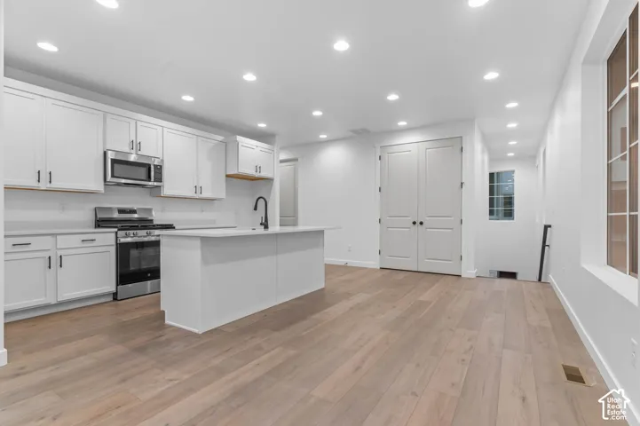 Kitchen featuring white cabinetry, wood-finish flooring, a central island, recessed lighting, and stainless steel appliances