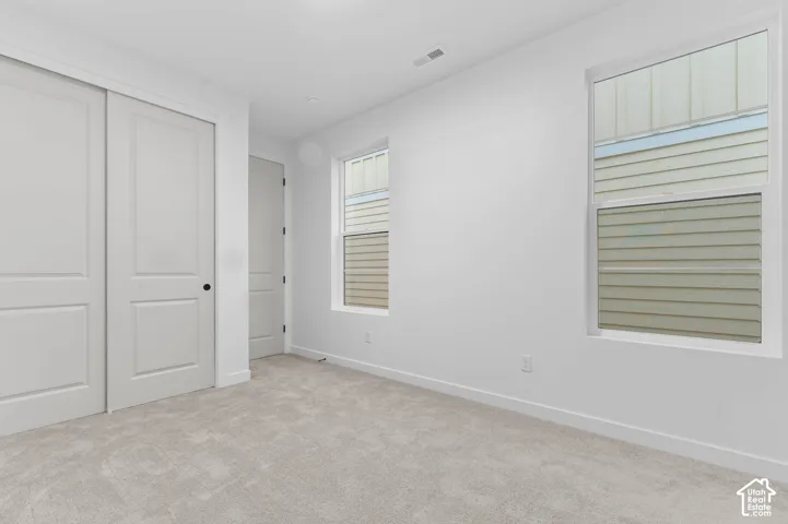 Neutral wall-to-wall carpeting, dual sliding closet doors with black hardware, and two double-hung windows
