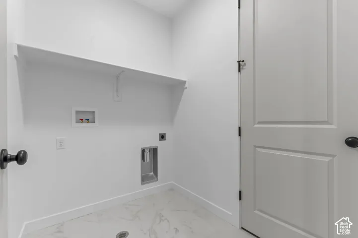 Utility room featuring stone-finish tile flooring, a recessed utility box with plumbing hookups, a built-in wall-mounted shelf, and a paneled interior door with matte black hardware