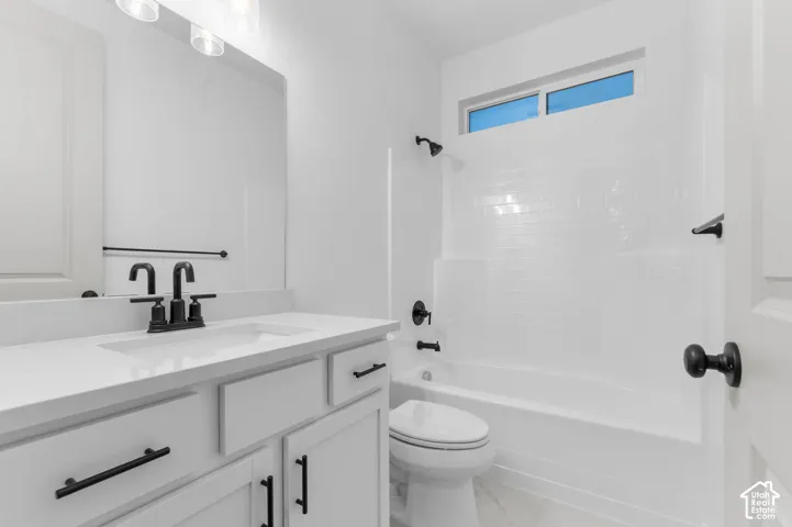 Bathroom featuring a white vanity with a solid-surface countertop, matte black hardware, a shower-tub combination with white subway-style tile surround, and a horizontal transom window
