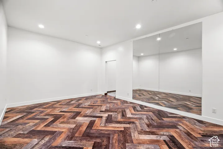 Interior space featuring wood-finish flooring in a herringbone pattern, floor-to-ceiling wall mirrors, and recessed ceiling lighting