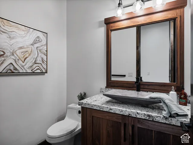 Custom wood-finish vanity with a stone countertop, vessel sink, matte black faucet, and matching framed mirror with integrated lighting