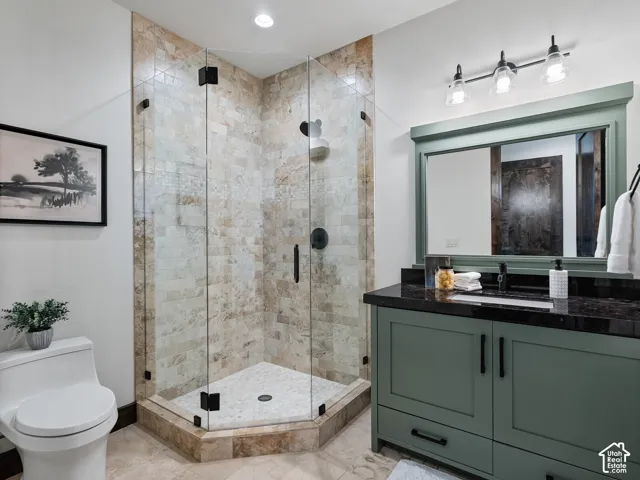 Custom vanity with a dark stone countertop, textured stone tile shower surround, frameless glass shower enclosure, recessed lighting, and integrated wall-mounted mirror with decorative trim