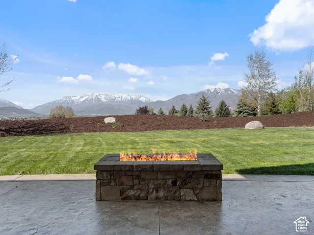 Custom rectangular outdoor stone fire pit situated on a stamped concrete patio, overlooking a manicured lawn and mountain backdrop