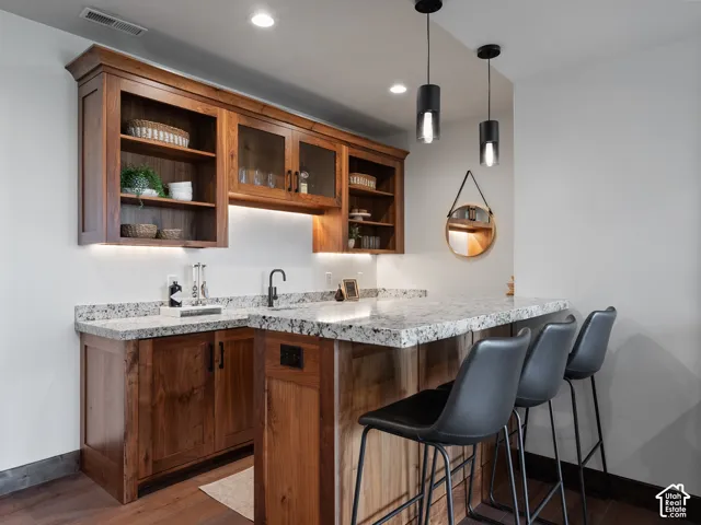 Custom wood cabinetry featuring glass-front uppers and integrated under-cabinet lighting, paired with natural stone countertops, a matte black faucet, and dual modern pendant fixtures
