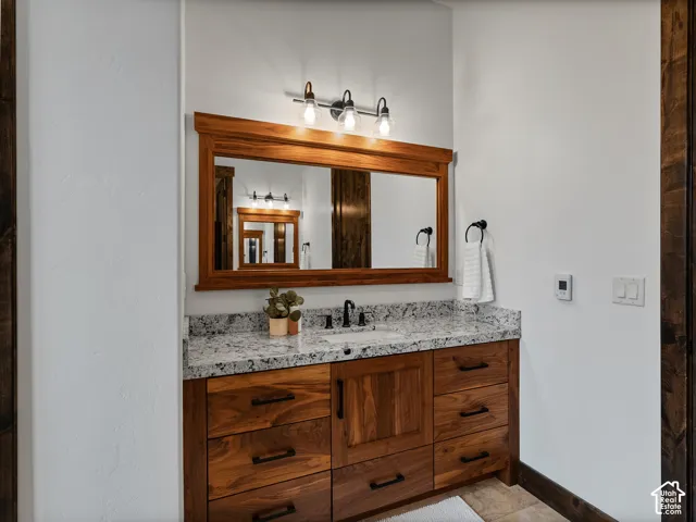 Custom wood vanity featuring stone countertop, integrated sink, matte black hardware, and matching wood-framed mirror with three-light fixture