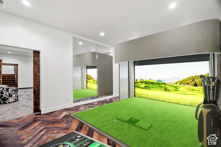 Dedicated golf simulator room featuring herringbone-pattern wood-finish flooring, floor-to-ceiling mirrored walls, and recessed lighting