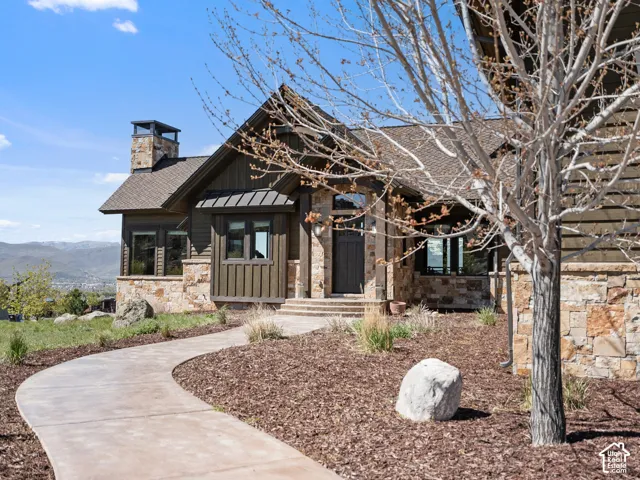 Craftsman-style exterior featuring vertical wood siding, natural stone accents, a concrete walkway, and a chimney stack