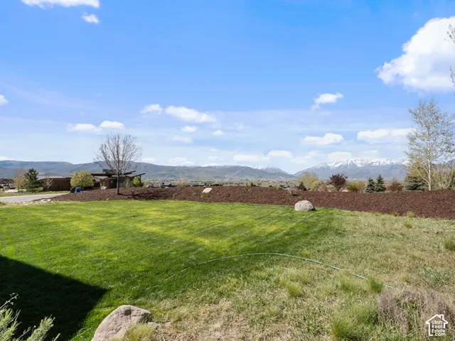 Expansive lawn featuring manicured turf, landscaped mulch beds, decorative boulders, and mountain scenery