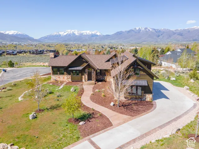 Custom exterior featuring horizontal wood-finish siding, stone masonry accents, a multi-pitched roofline with metal detailing, and a concrete driveway leading to a stone-paved walkway, set against a backdrop of snow-capped mountains