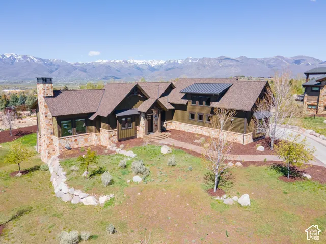 Custom exterior featuring stone and siding, multi-pitched rooflines with metal accents, an expansive stone chimney, and mountain scenery